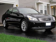 a black car parked in front of a house on a wet driveway with green grass