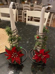 two candles are sitting on top of a table with christmas decorations and greenery in them