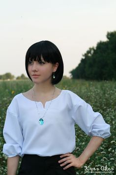 a woman standing in a field with her hands on her hips wearing a white blouse and black pants