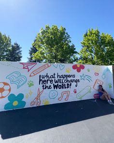 a woman sitting on the ground in front of a sign that says, what happens here will change the world