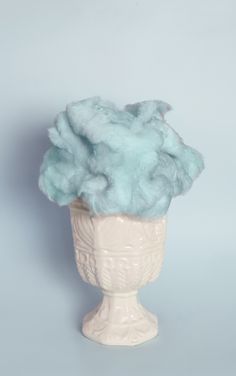 a white vase filled with blue wool on top of a table