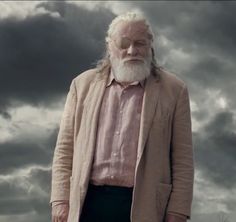 an old man with white hair and beard standing in front of dark clouds