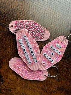 three pink key chains with words on them sitting on a table next to each other