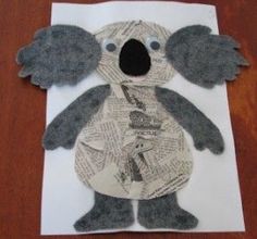 a koala made out of newspaper sitting on top of a wooden table next to a piece of paper