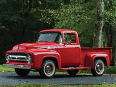 an old red pickup truck parked in front of trees