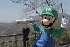 a man dressed as mario is standing next to a parking meter with his hands in the air