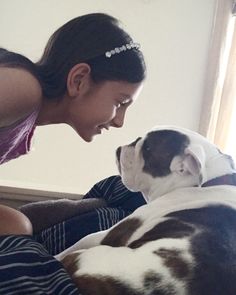 a woman petting a dog laying on top of a bed next to a window