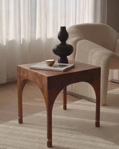a table with a vase on top of it in front of a chair and window