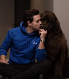 a man sitting on the floor with his dog and kissing him in front of him