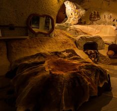 there is a cave like room with stone walls and rock formations on the wall, as well as an animal skin covered bed