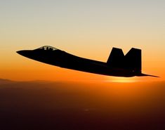 a fighter jet flying through the air at sunset