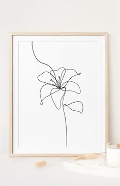 a black and white drawing of a flower in a frame next to a candle on a table