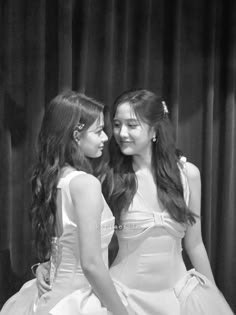 two young women standing next to each other in front of a curtain with their backs turned