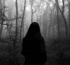 a woman standing in the woods with her back to the camera, looking at trees and fog