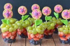 small cups filled with fruit and flowers on top of a wooden table next to cookies