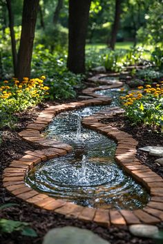 a brick path that leads to a water feature in the middle of a garden with flowers and trees