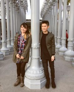 two people standing next to each other under a light pole with columns in the background