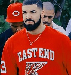a man with a beard wearing an orange shirt and red baseball cap standing in front of other men