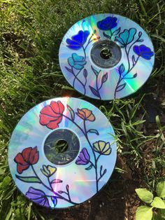 two cds sitting in the grass with flowers painted on them