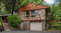 a stone house with two garages in front of it and trees around the building