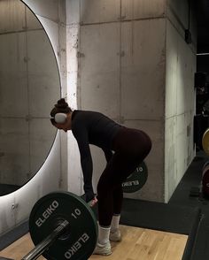 a woman squatting down with a barbell in front of her and looking into the mirror
