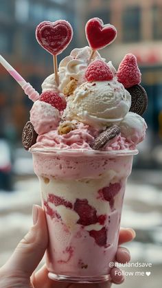 a person holding up a cup filled with ice cream and toppings on top of it