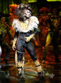 a woman in costume standing on stage with other people behind her