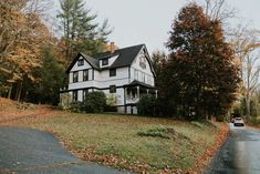 a white house sitting on the side of a road in front of trees and grass
