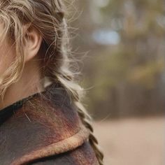 a woman with blonde hair and braids on her head looking off into the distance