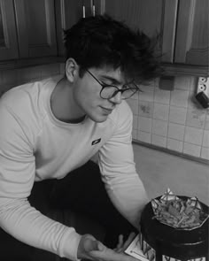 black and white photograph of a young man in glasses leaning over a cake with french fries on it