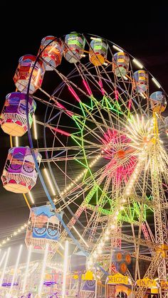 a ferris wheel at night with lights on it's sides and carnival rides in the background