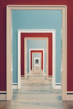 an empty hallway with red, blue and white walls in the center is seen through two doorways
