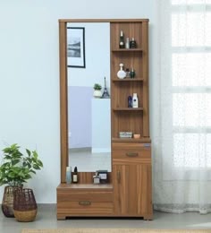 a wooden cabinet sitting next to a mirror on top of a floor near a potted plant