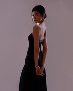 a woman in a black dress is standing with her hand on her hip and looking away from the camera