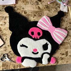 a black and white cat rug with pink bows on it's head, sitting next to a pair of scissors
