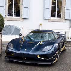 a blue and gold sports car parked in front of a white building with shutters