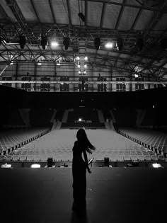 black and white photograph of a woman standing in front of an empty stadium with lights on the ceiling