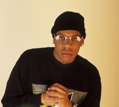 a man wearing glasses and a black sweater is posing for the camera with his hands on his chest