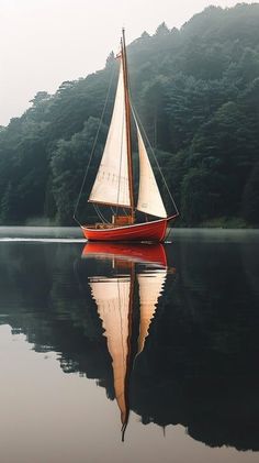 a red sail boat floating on top of a lake