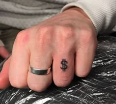 a person's hand with a small tattoo on it and a dollar sign tattooed on the middle finger
