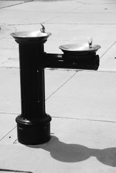 a black and white photo of a water fountain on the side of the street with two sinks in it
