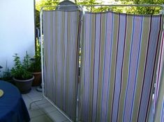 an outdoor shower with striped fabric on the side and blue table cloth on the other side