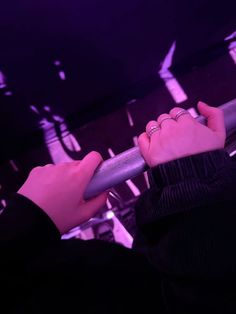 a person holding onto a metal pole with their hand on the rail and purple lights in the background