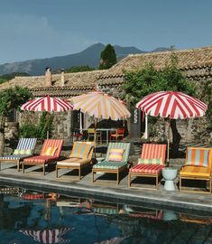 chairs and umbrellas are lined up next to the pool in front of an old stone house