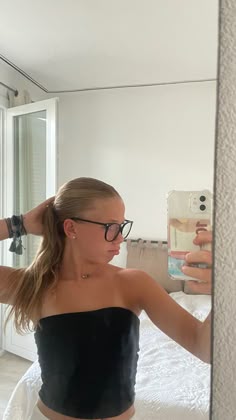 a woman taking a selfie in the mirror with her cell phone and wearing glasses