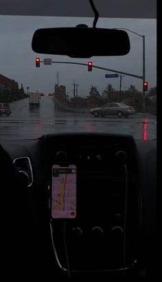 the dashboard of a car on a rainy day with red traffic lights and street signs
