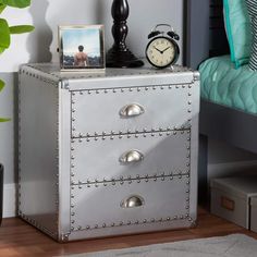 a nightstand with two drawers and an alarm clock on the top, next to a bed