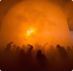 a group of people standing in the fog with their arms up and one person pointing at something