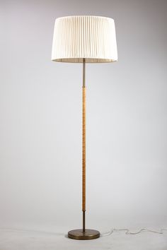 a wooden floor lamp with a white shade on the base and a cord attached to it