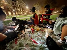 people sitting on the grass with laptops and papers in front of them at night